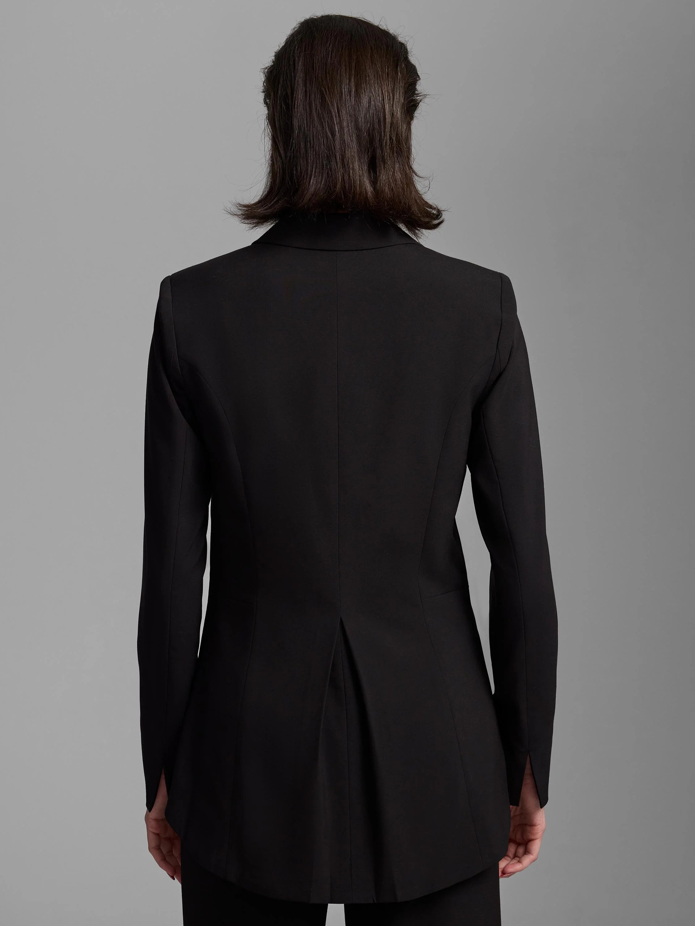 Black tailored blazer, back view. Features center seam, single back vent, and long sleeves with slit cuffs.