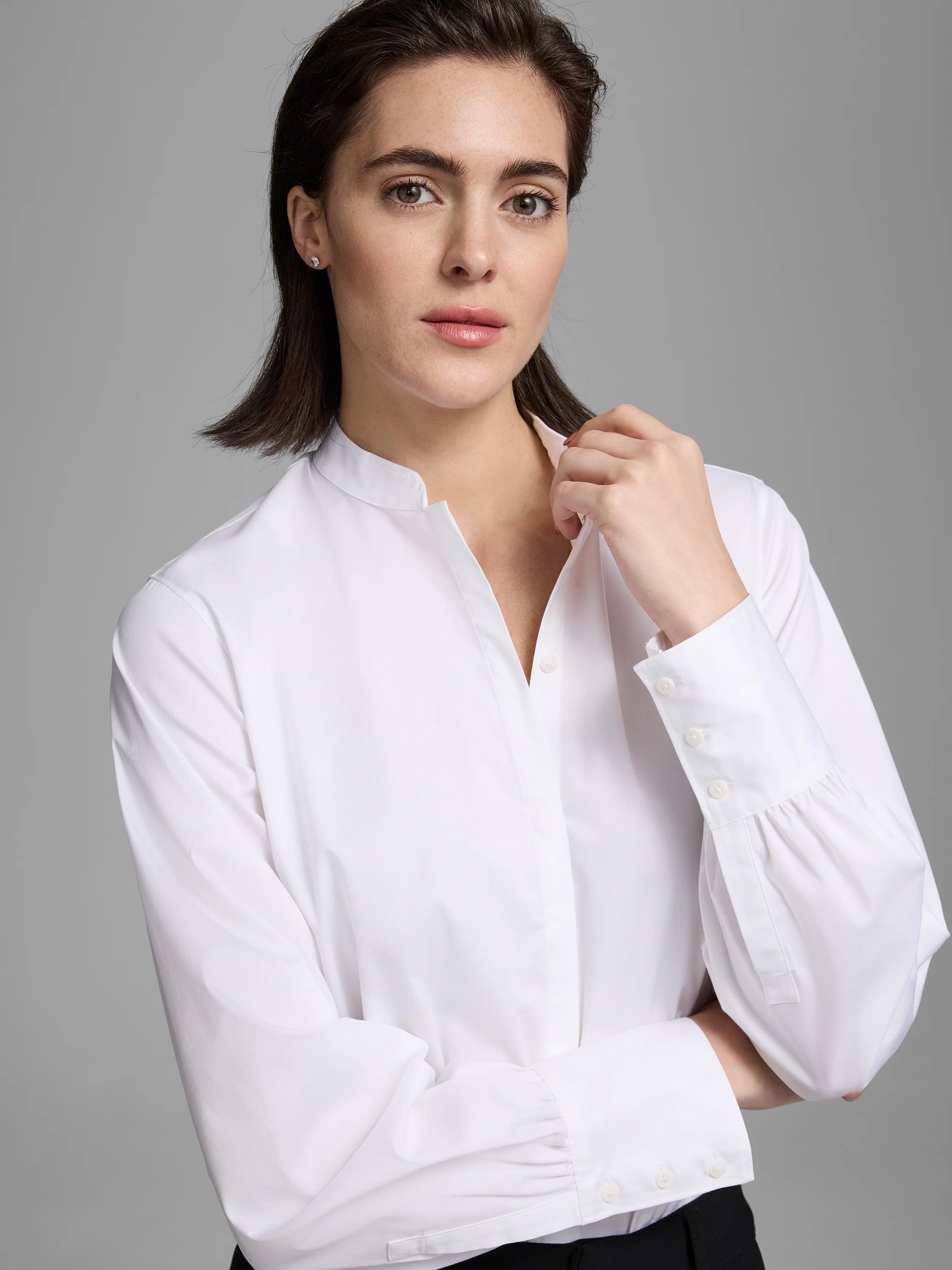 White shirt with band collar, partial button placket, and long sleeves with gathered three-button cuffs.