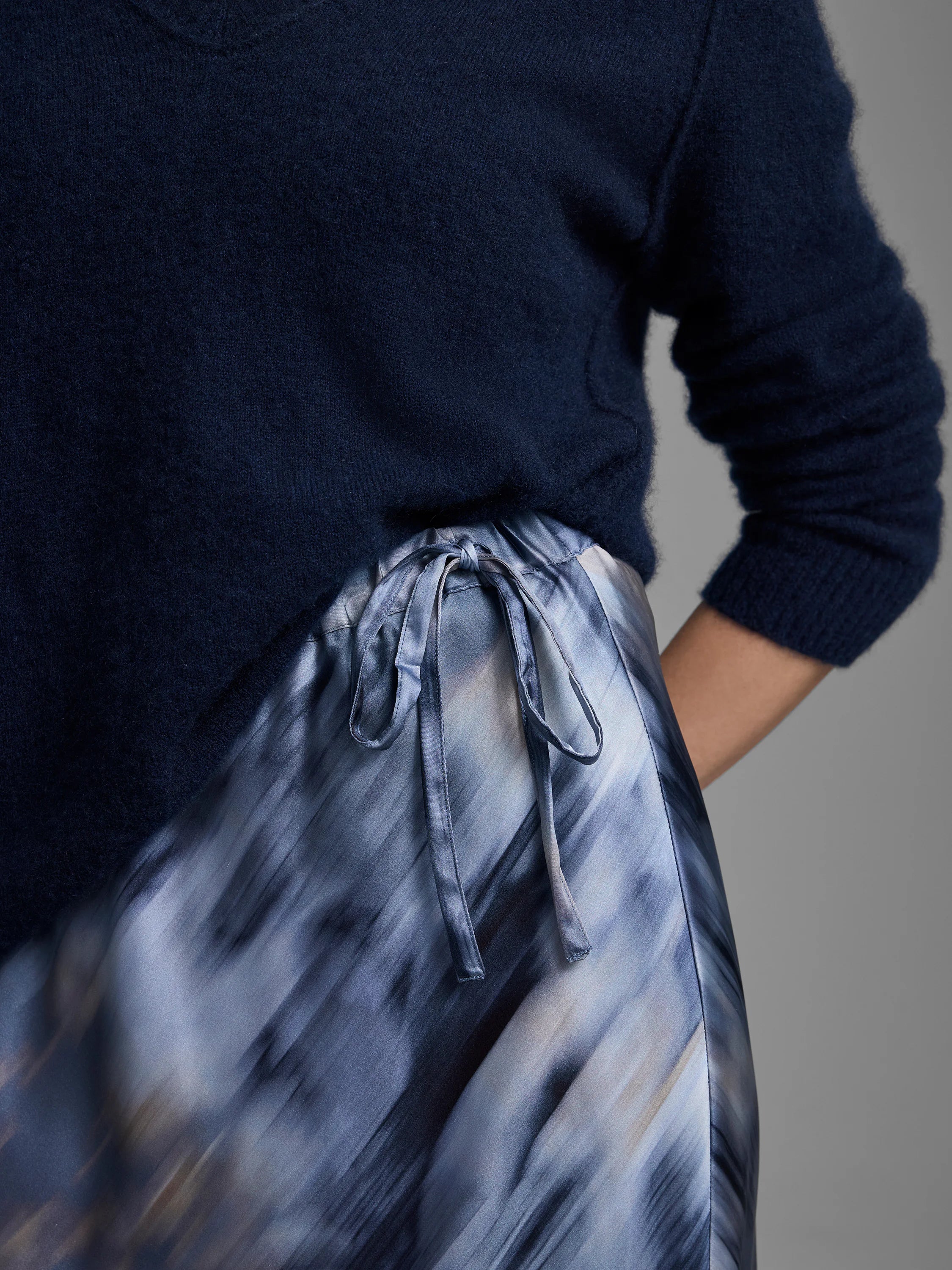 Silk slip skirt with an abstract streaky pattern in shades of blue, gray, and beige, with a tied waist.