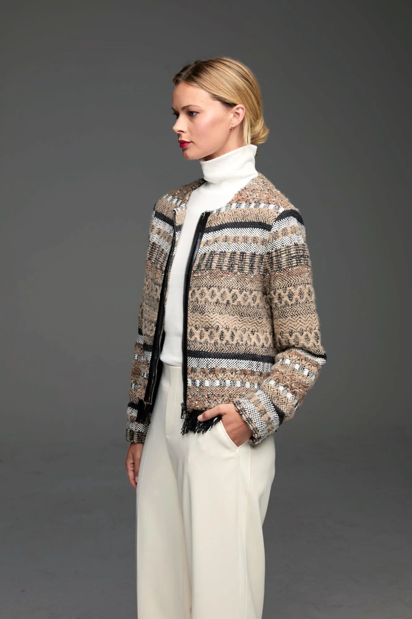 Knit jacket with beige, white, black woven patterns & textures. Features a black zippered front and black fringe hem.