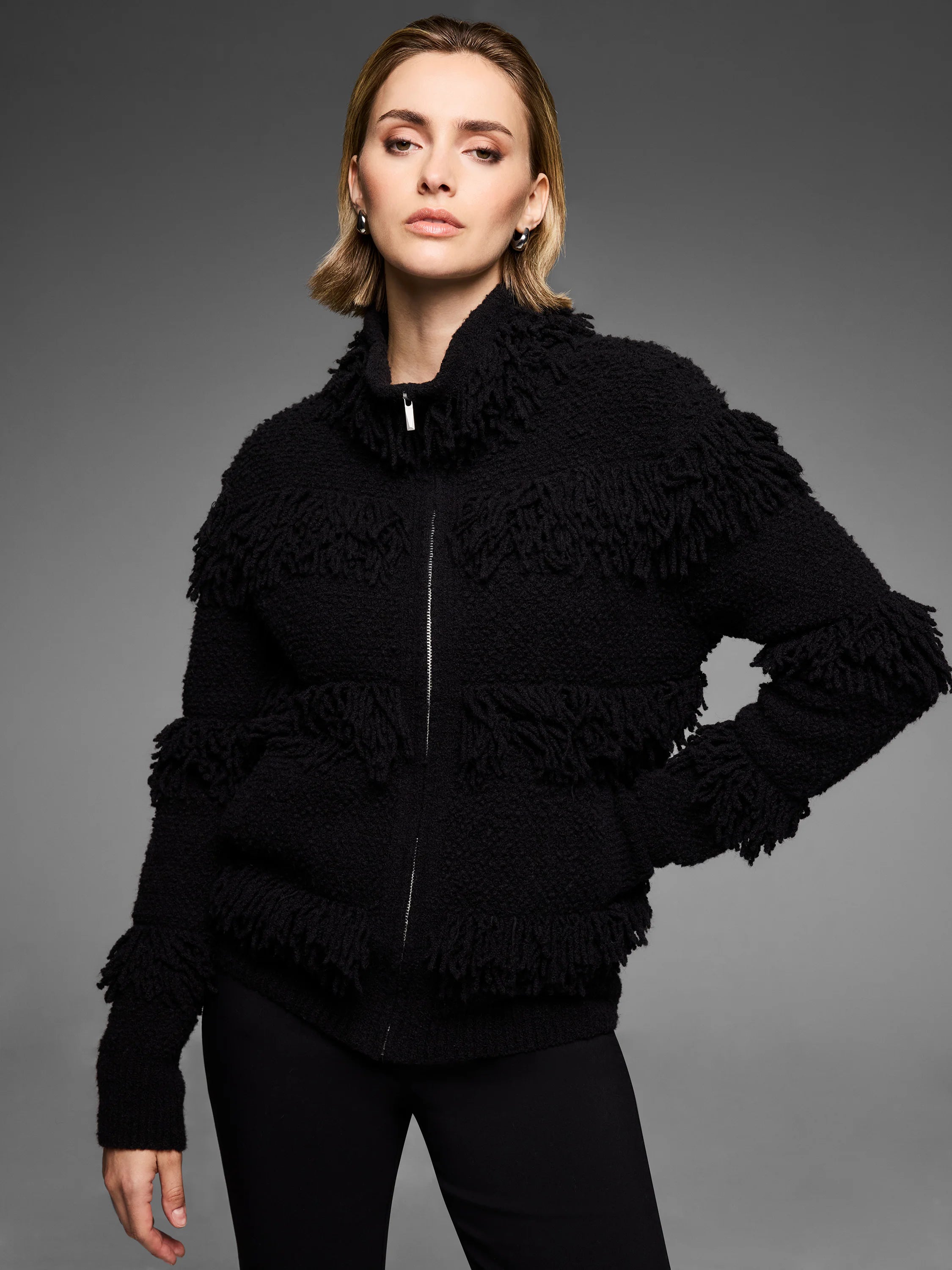 Black full-zip jacket with horizontal placed fringe. Features a silver zipper and stand collar.