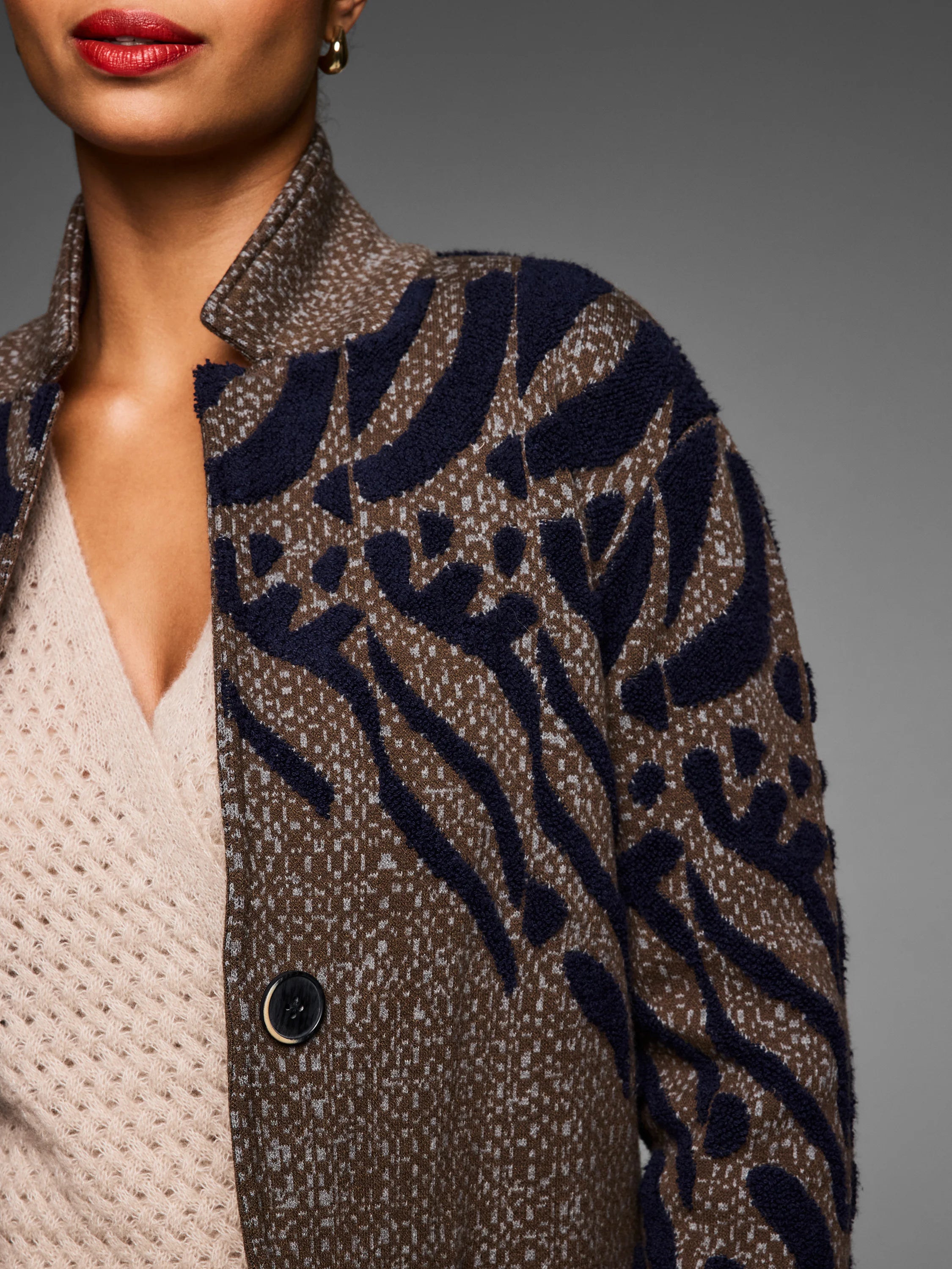 Brown double-knit coat with light flecks, features raised navy blue abstract patterns and one black button.