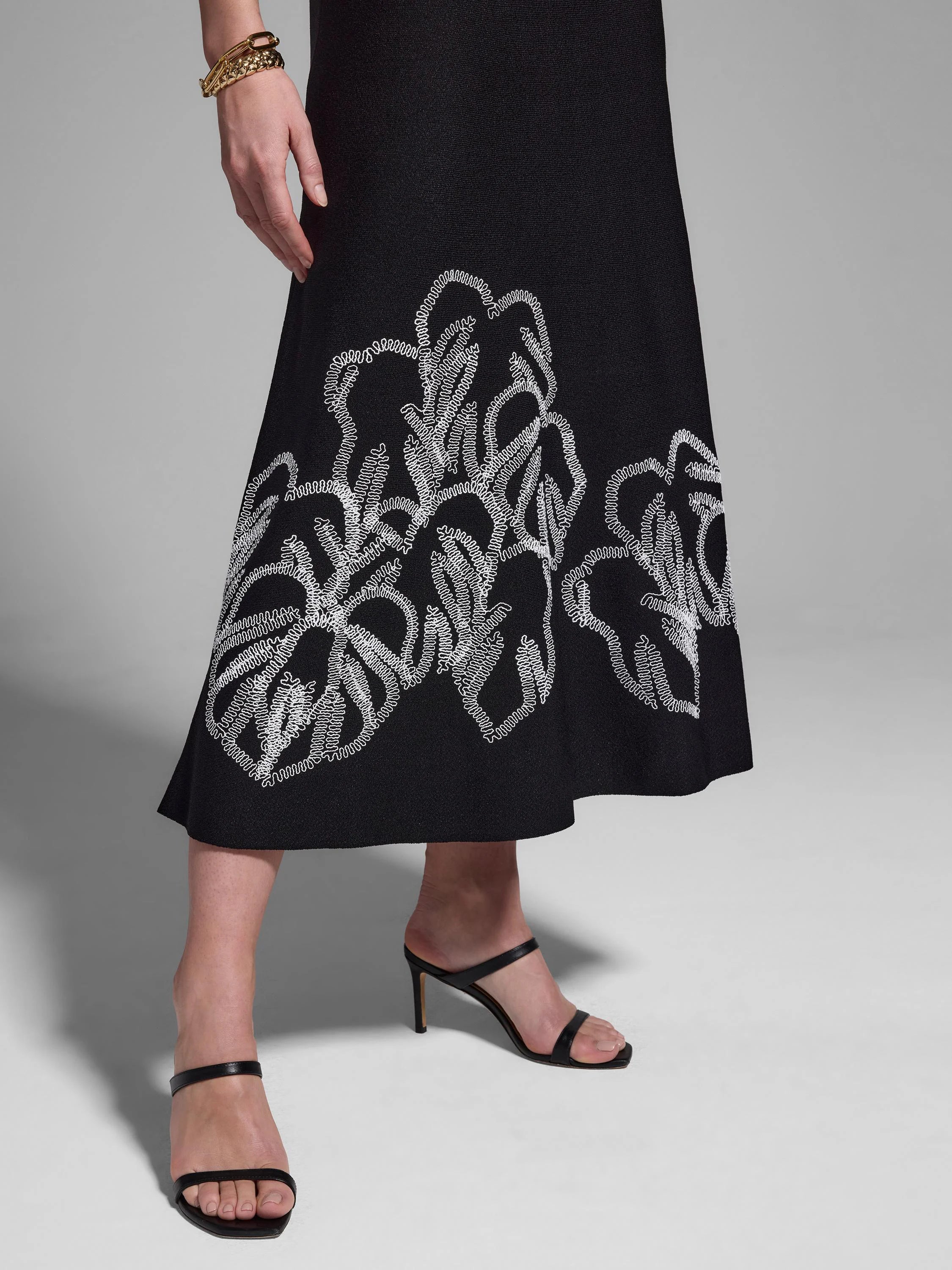 Black midi dress with white embroidered leaf pattern at hem.
