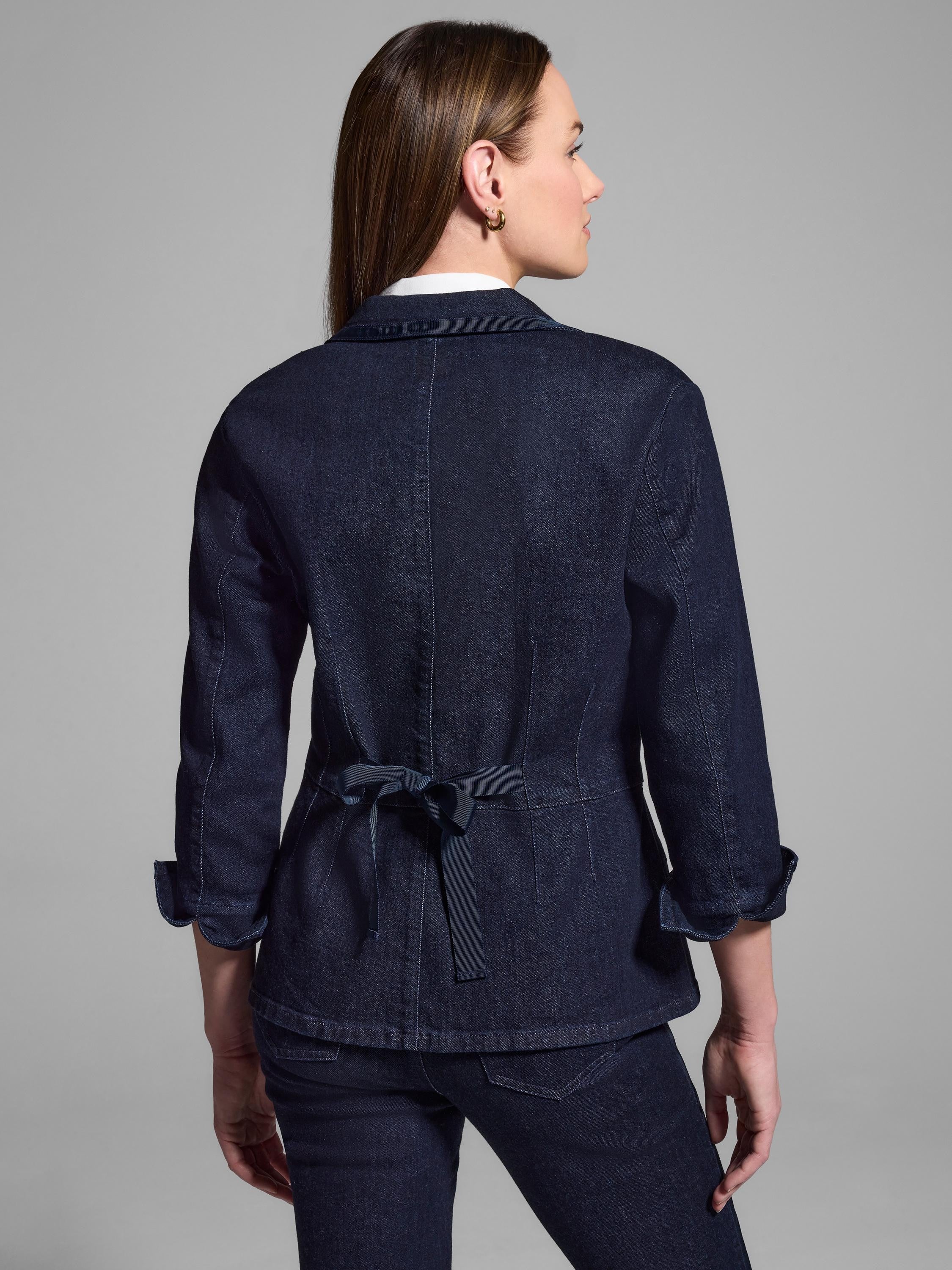 Dark wash denim blazer, back view. Features a black ribbon tie at the waist. The sleeves are three-quarter length.