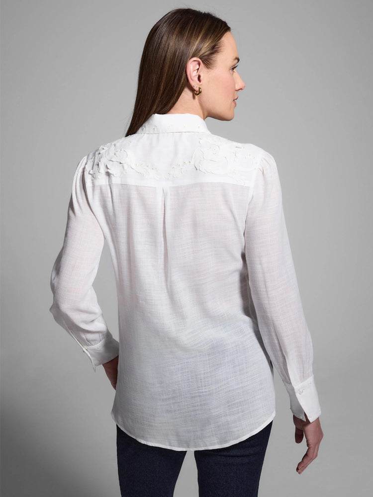 White long-sleeve collared shirt with white embroidered floral detailing and pearl accents on yoke and cuffs. Back view.
