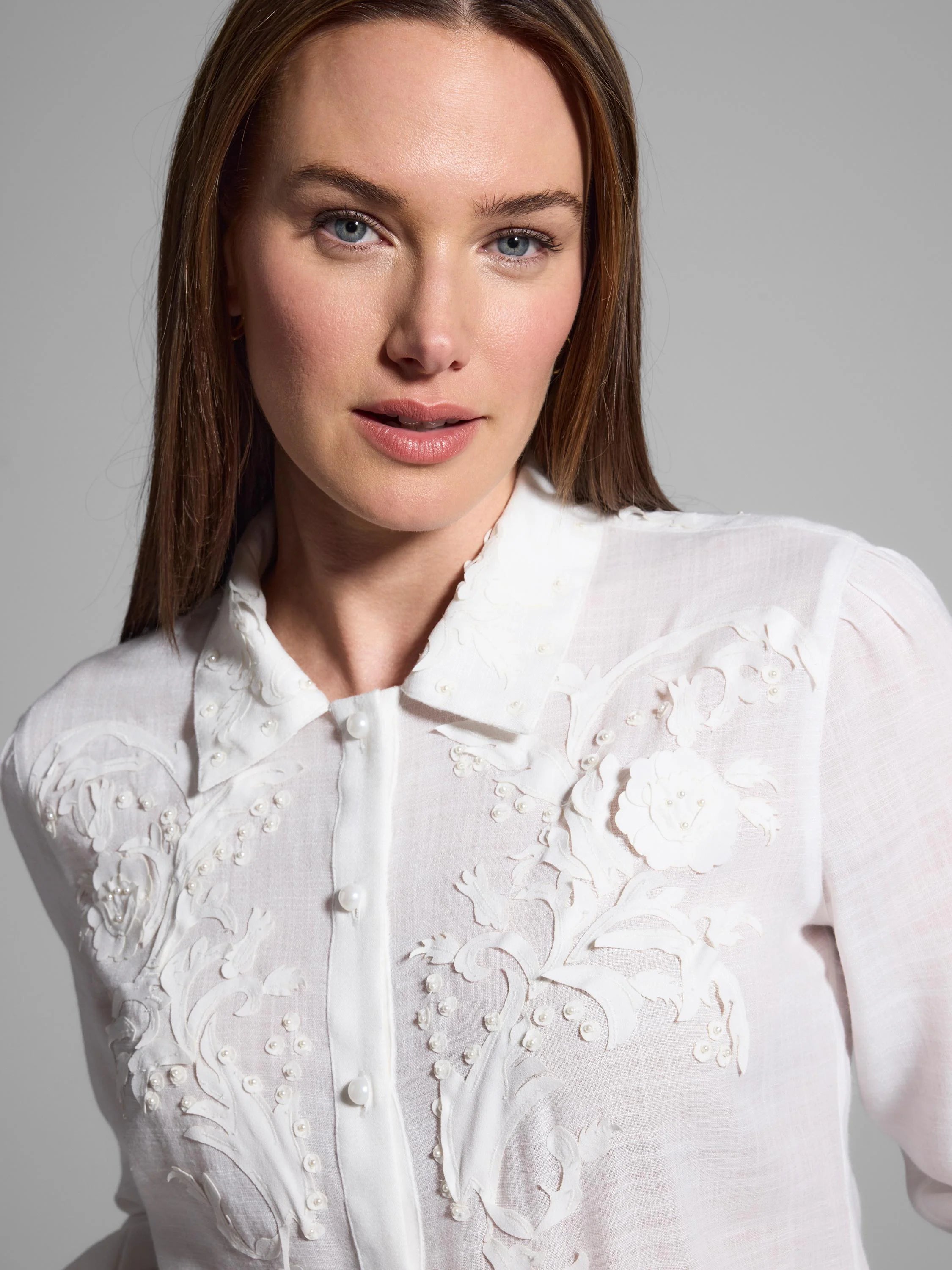 White collared shirt with ornate white floral embroidery and pearl accents.
