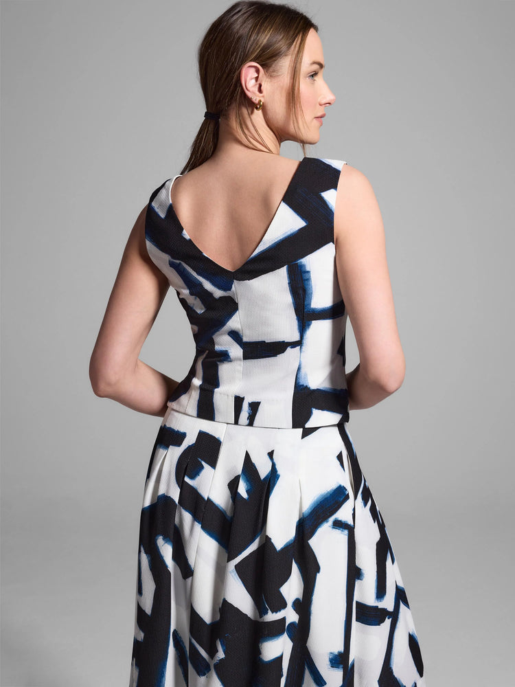 White top and skirt with an abstract blue and black print. Sleeveless top, V-neck back. Pleated skirt.