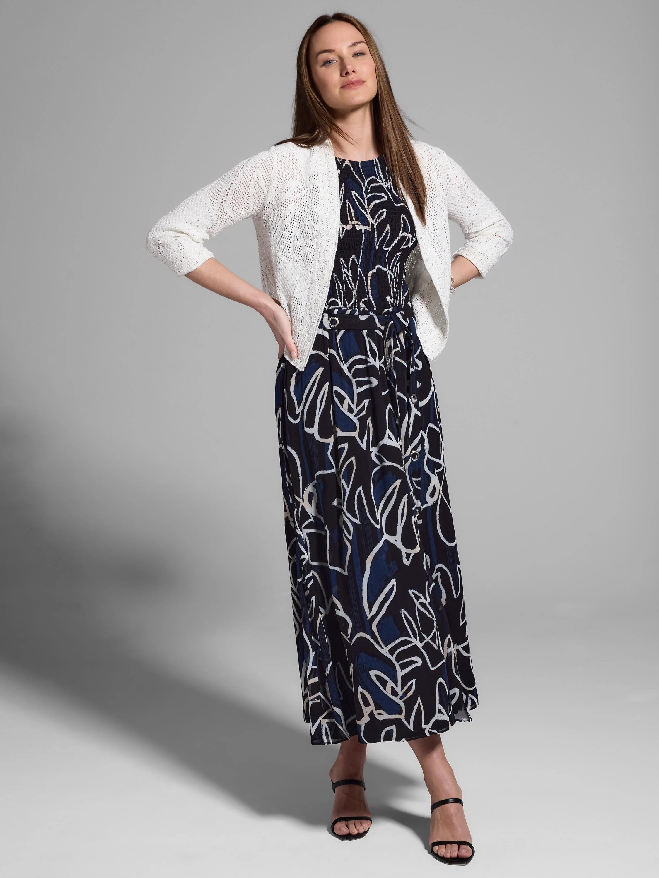 Off-white open cardigan over a navy and white abstract print maxi dress.