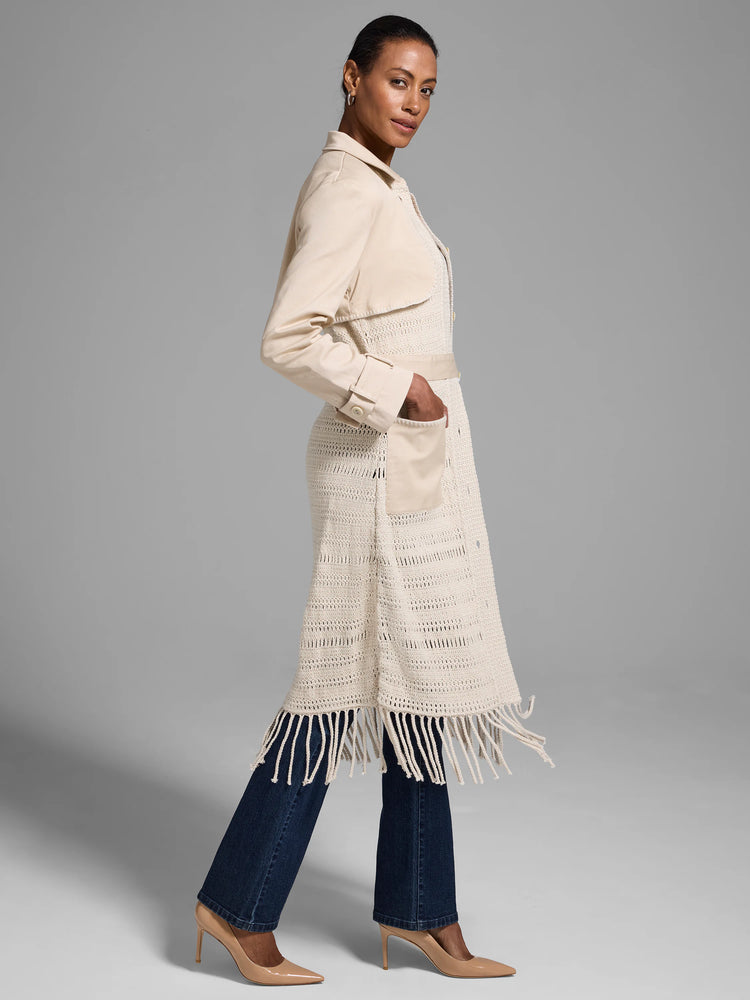 Beige knit jacket with fringe, cream-colored woven top section, and long sleeves. Features a belted waist and pockets.