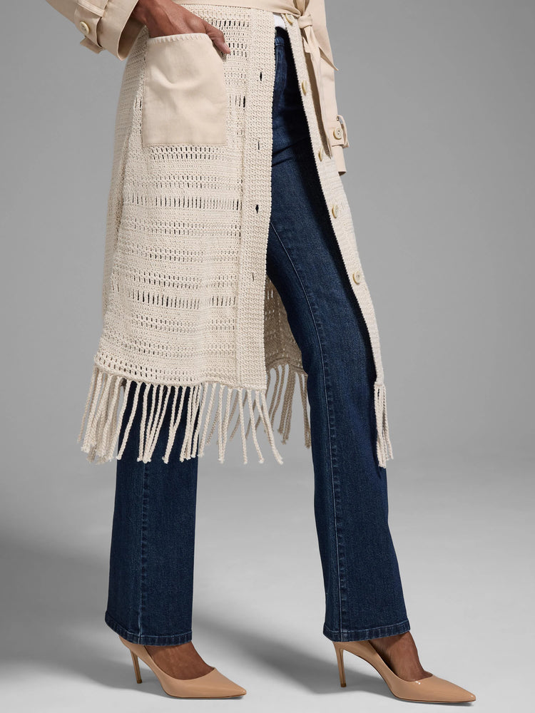 Beige open-knit jacket with fringe, button front, and patch pocket. Dark wash jeans and beige heels shown.