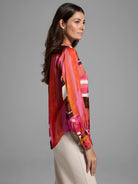 Glossy blouse with abstract orange, pink, and brown brushstroke pattern. Long sleeves, button cuffs.