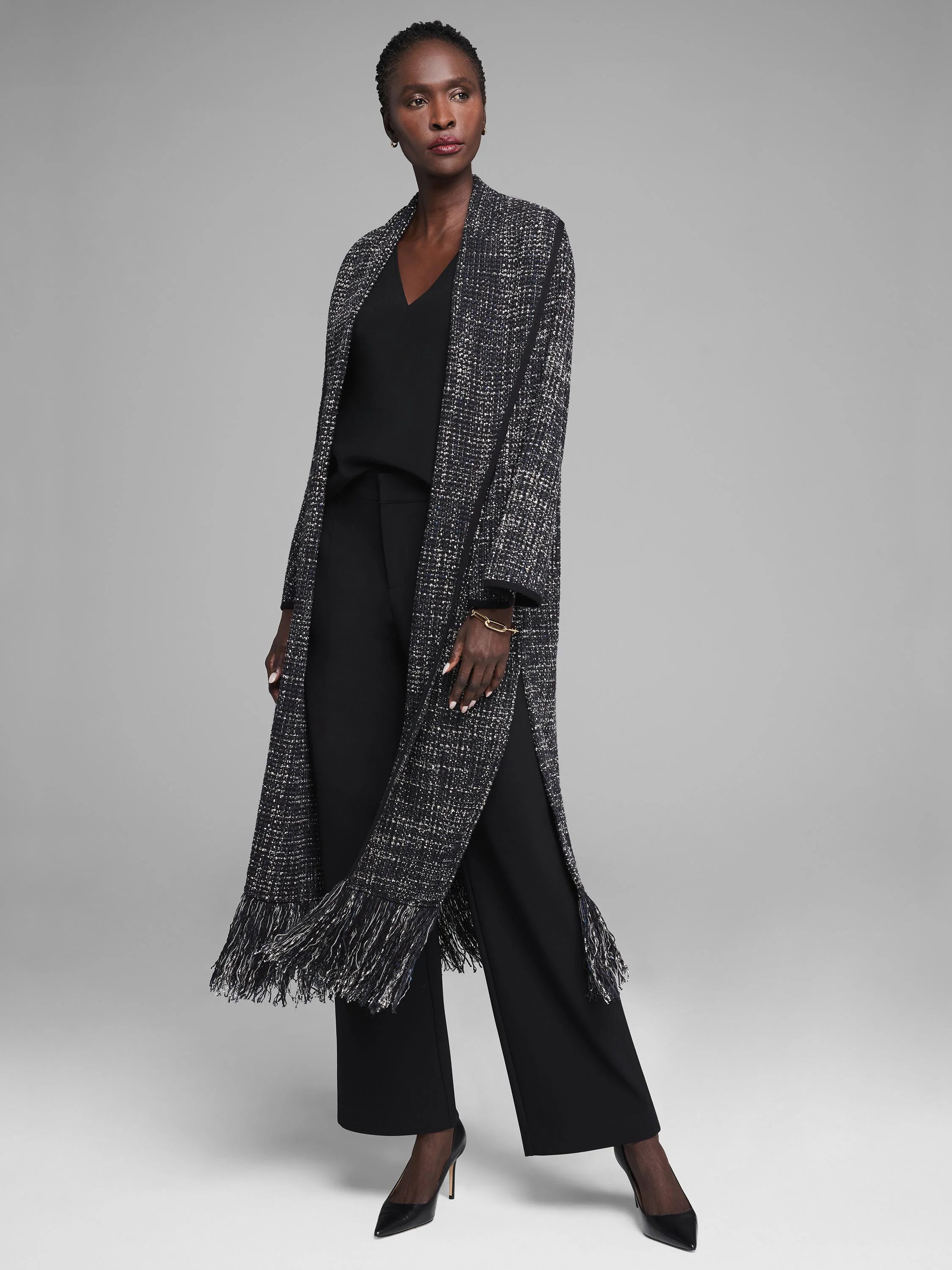 Long black, white, and gold tweed-texture jacket with fringe along the hem and high side slits.