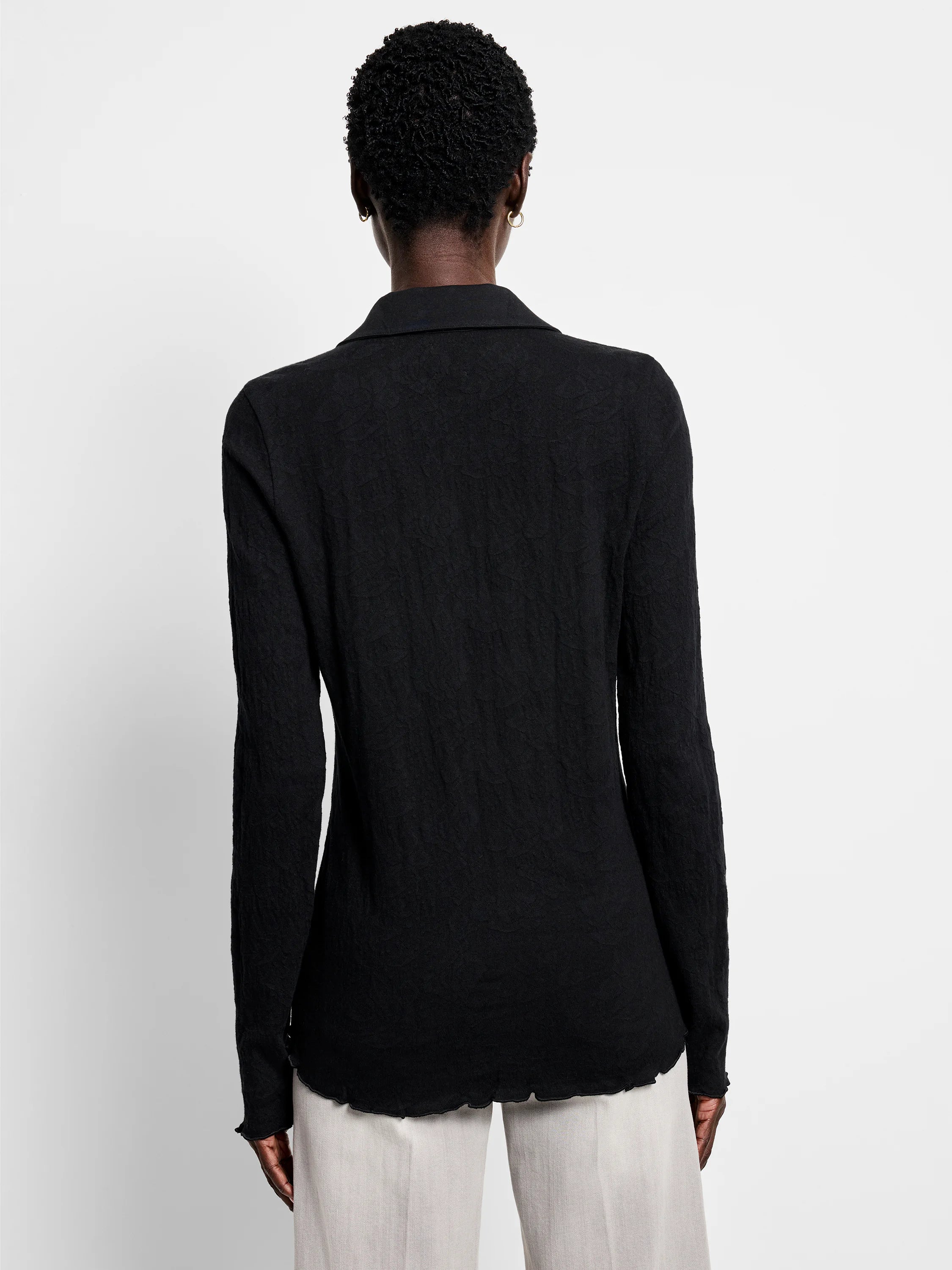 Back of black collared lace-knit top. Long sleeves, wavy lettuce-edge cuffs and hem.
