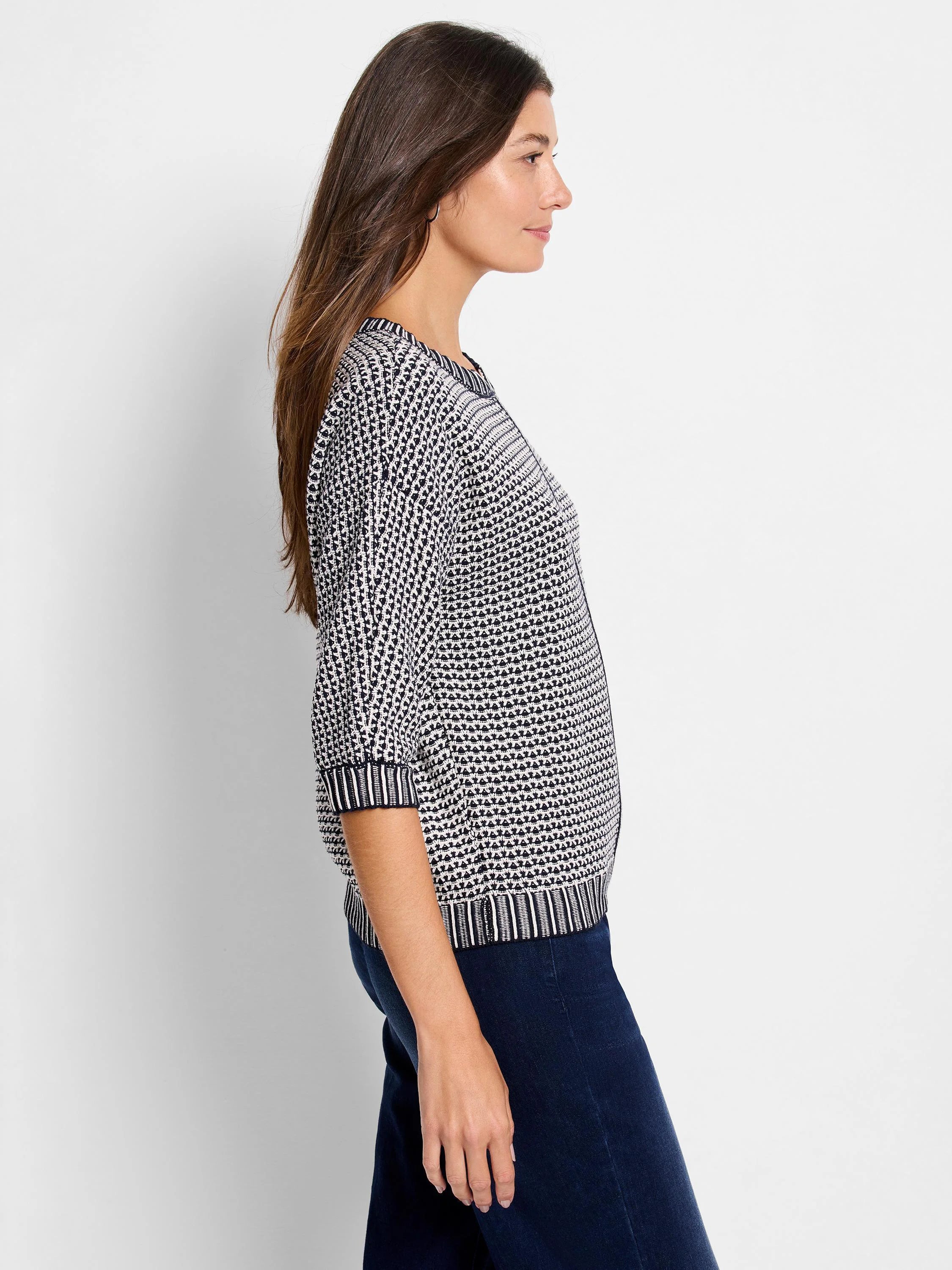 Black and white geometric tuck stitch sweater with elbow sleeves. Features striped neckline, cuffs, and hem.