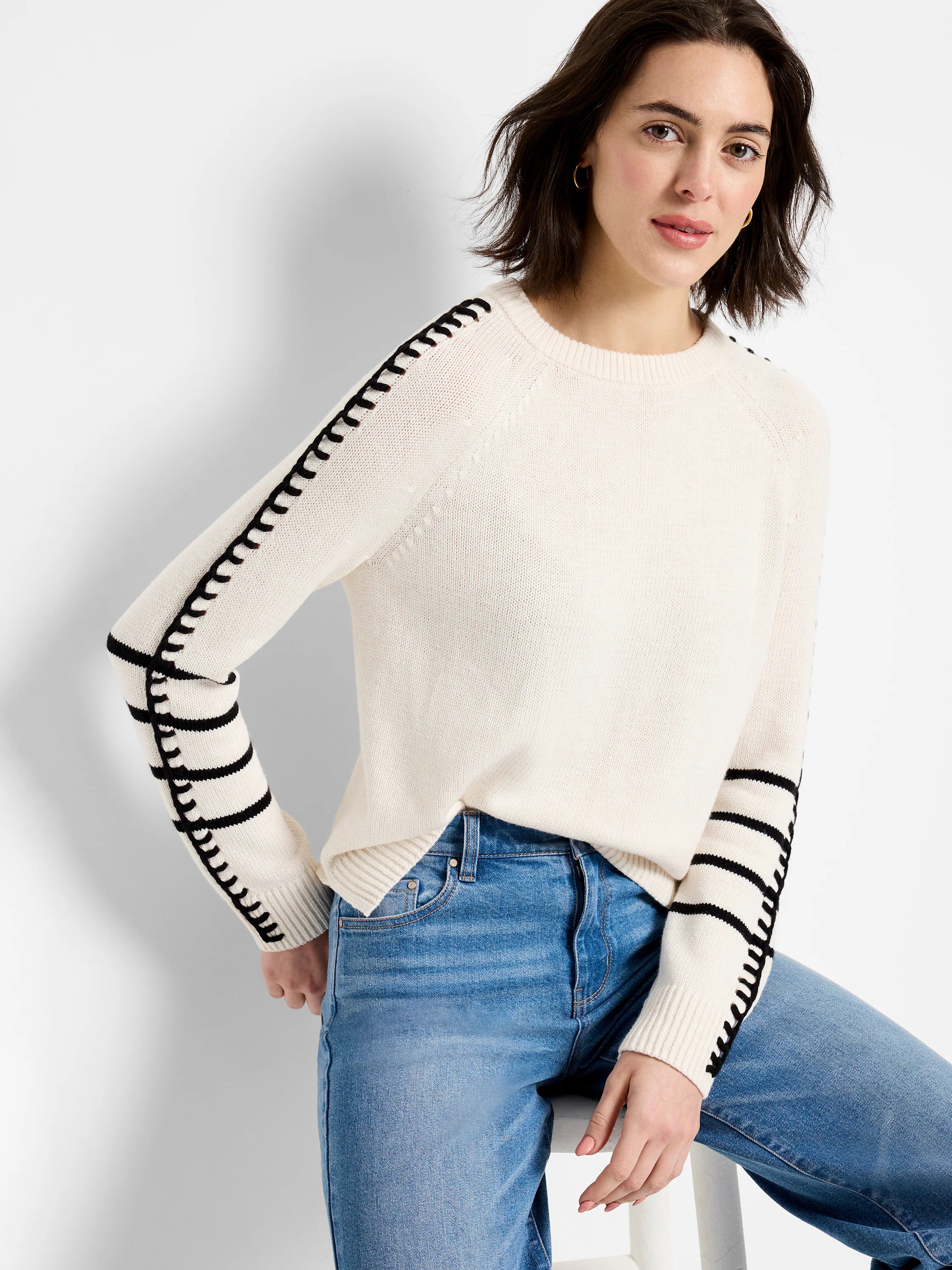 Off-white sweater with black stitching along raglan seams and horizontal black stripes on the lower sleeves.