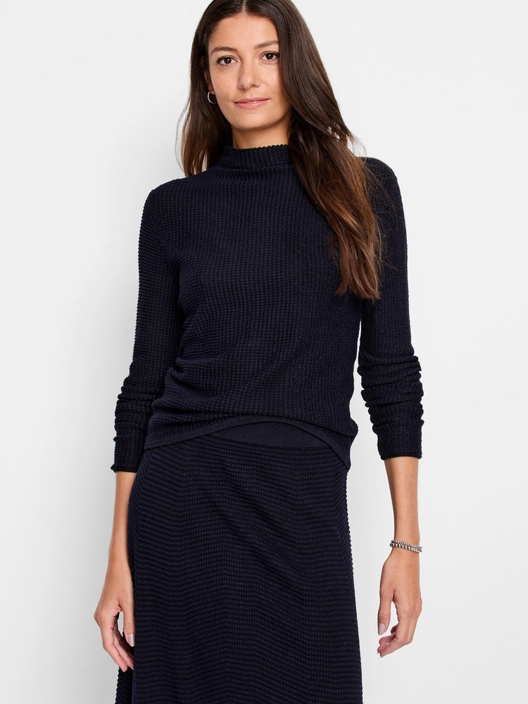 Woman wearing a dark blue pixel knit sweater with a high neck, long sleeves, and a waffle-knit texture.
