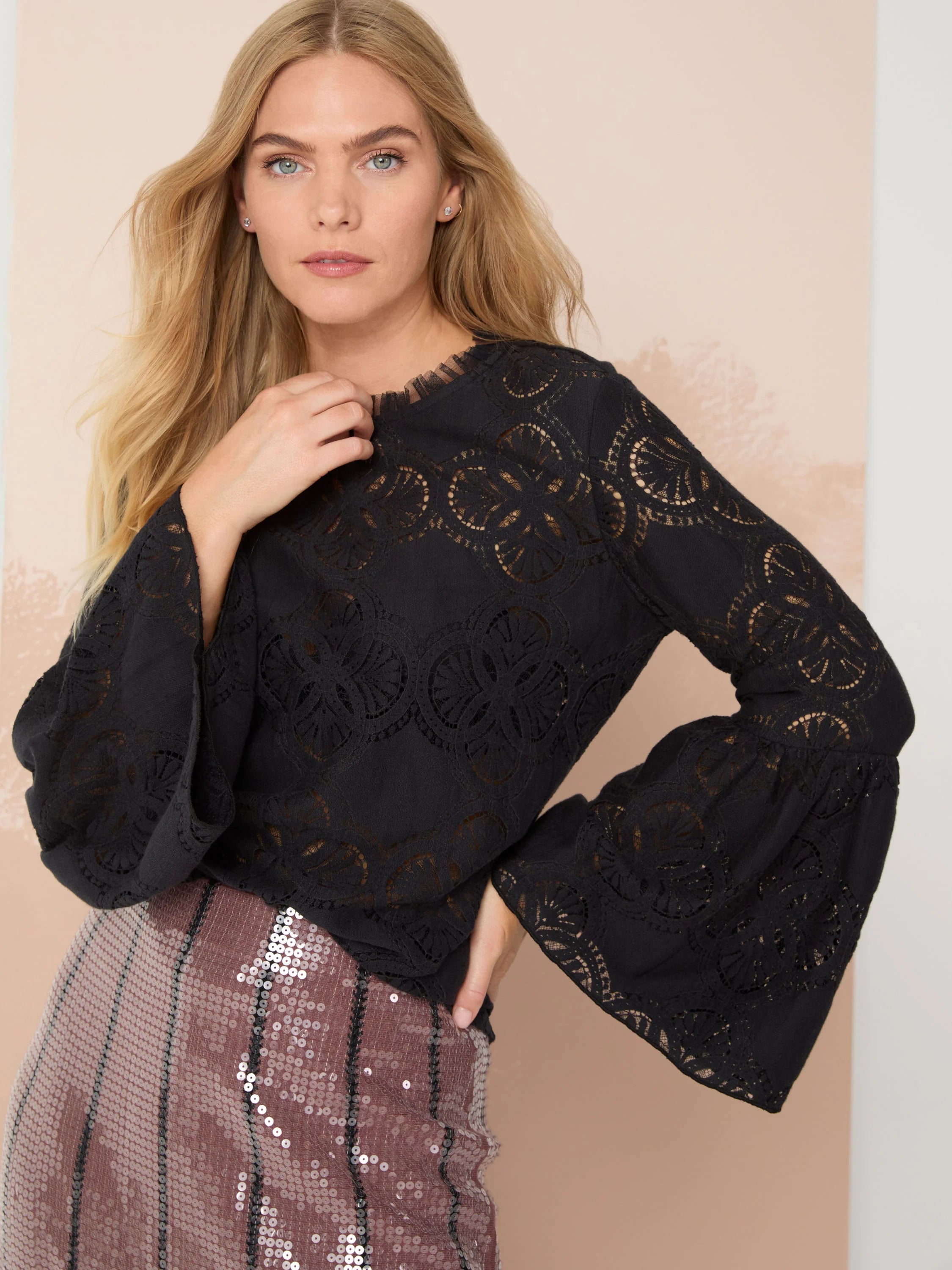 Black lace top with bell sleeves and repeating floral pattern. Round neckline.