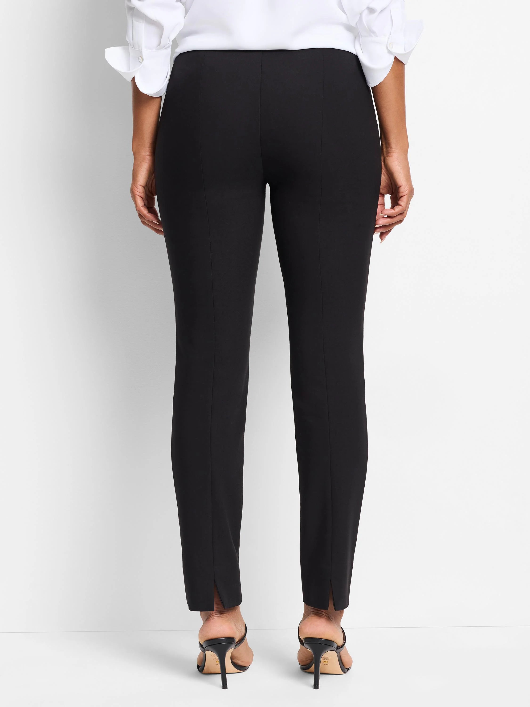 Black slim-fit pants, center seam detail, slight side slits at hem. Shown with black heels.
