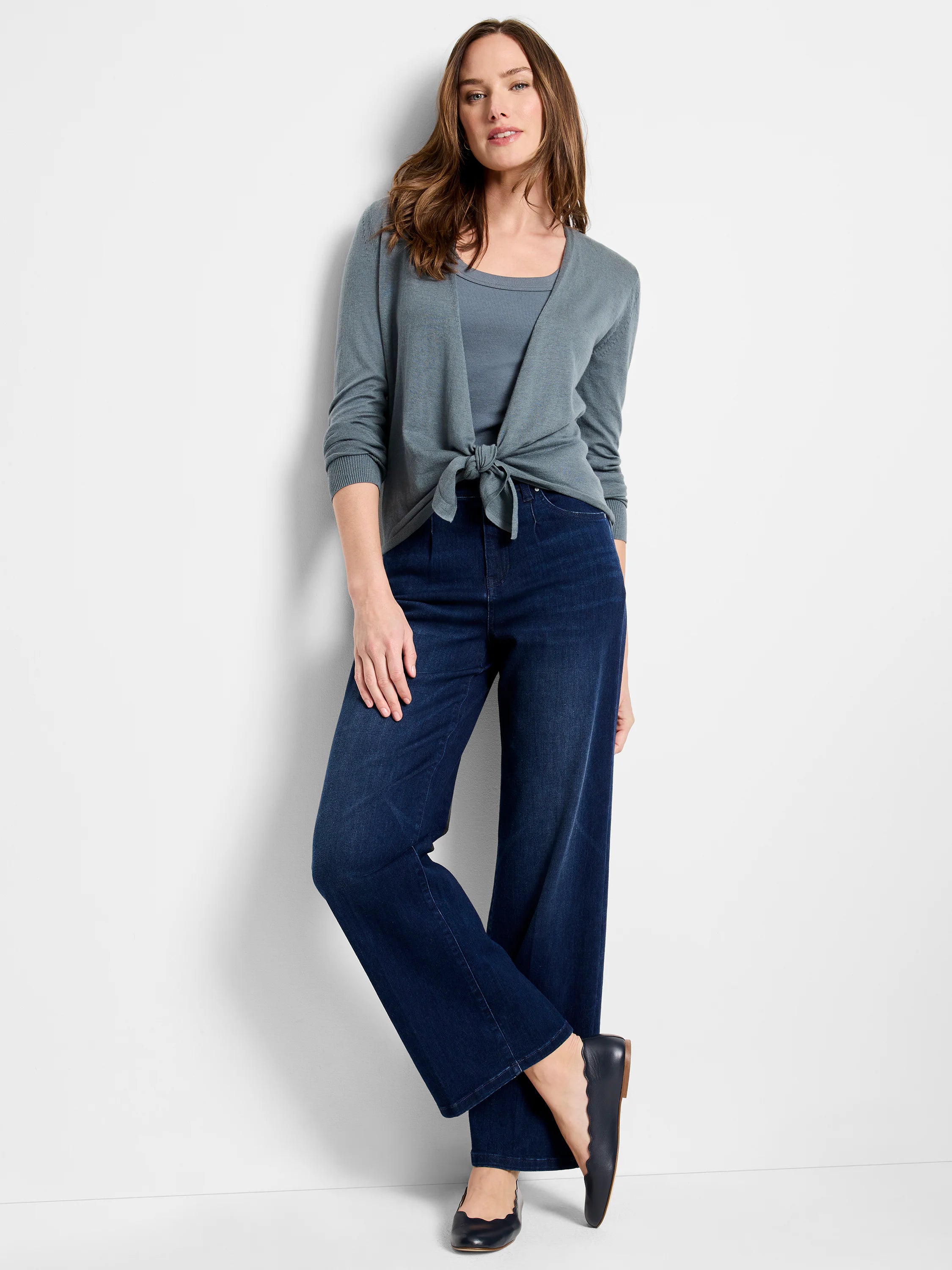 Dark wash wide-leg jeans on a model. The jeans are dark blue. The model also wears a grey cardigan and dark flats.