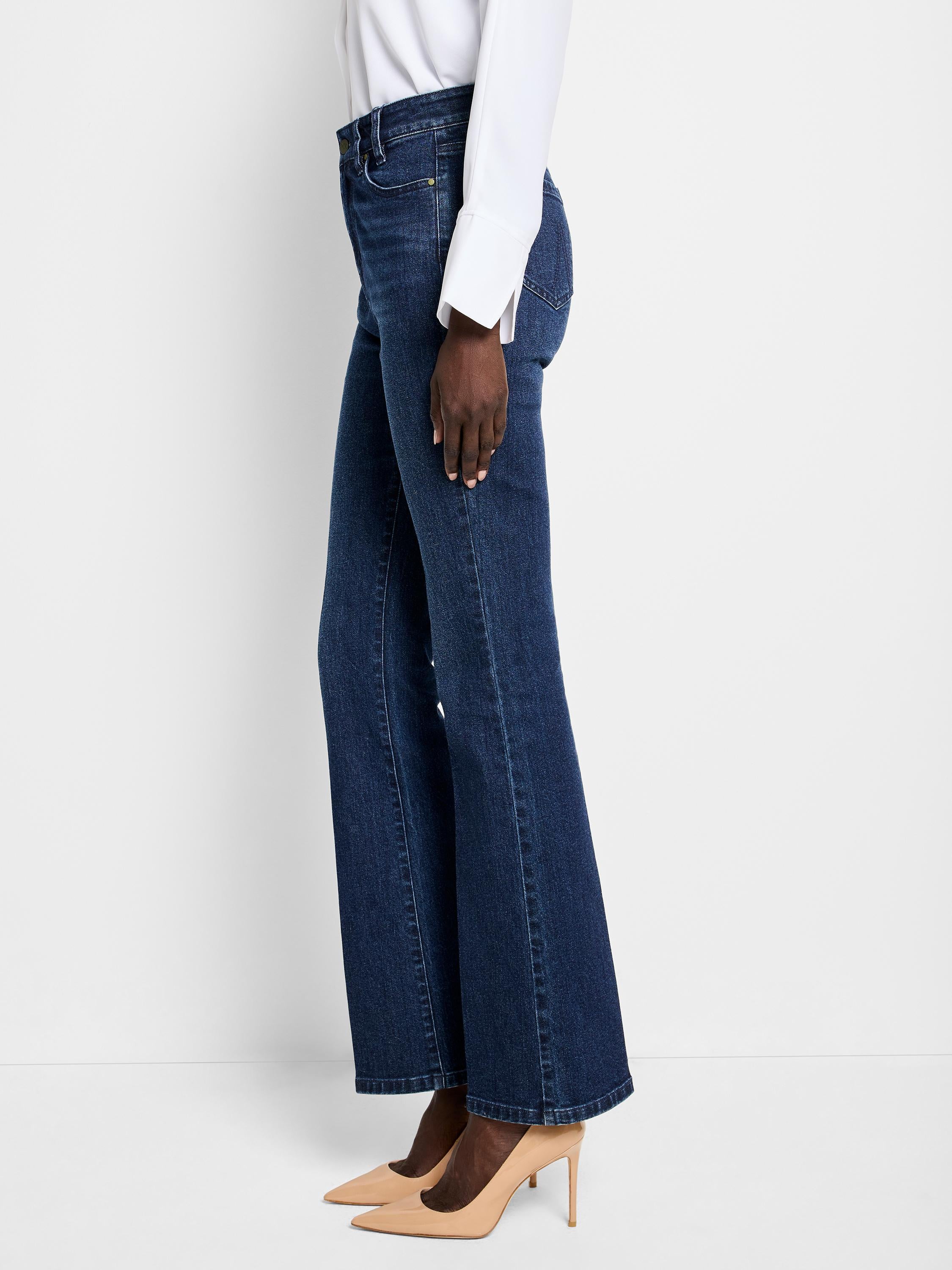 Dark blue denim flare jeans are worn high-waisted, fitting slim through the thigh with a wide bootcut leg opening.