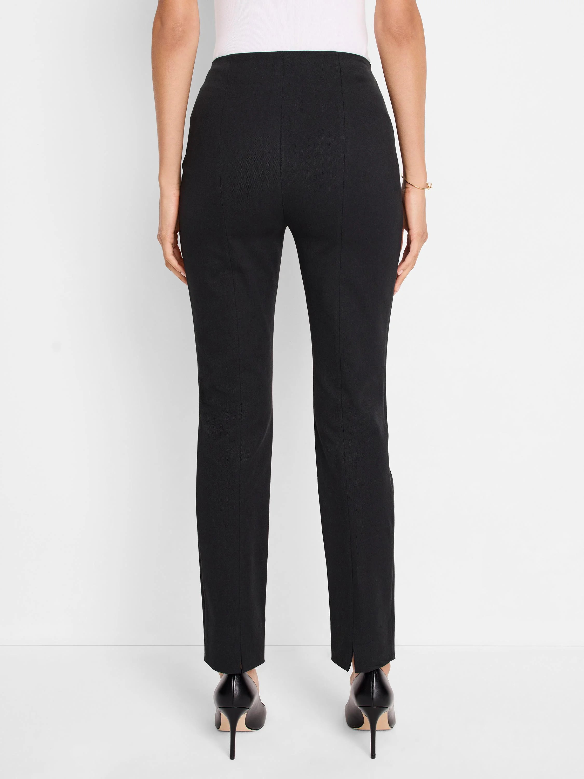 Black slim-leg pants, center back view. Vertical seams visible. Slight slits at the hem.