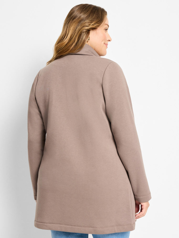 Light brown, tunic-length jacket with a stand collar and long sleeves, modeled by a woman facing right.