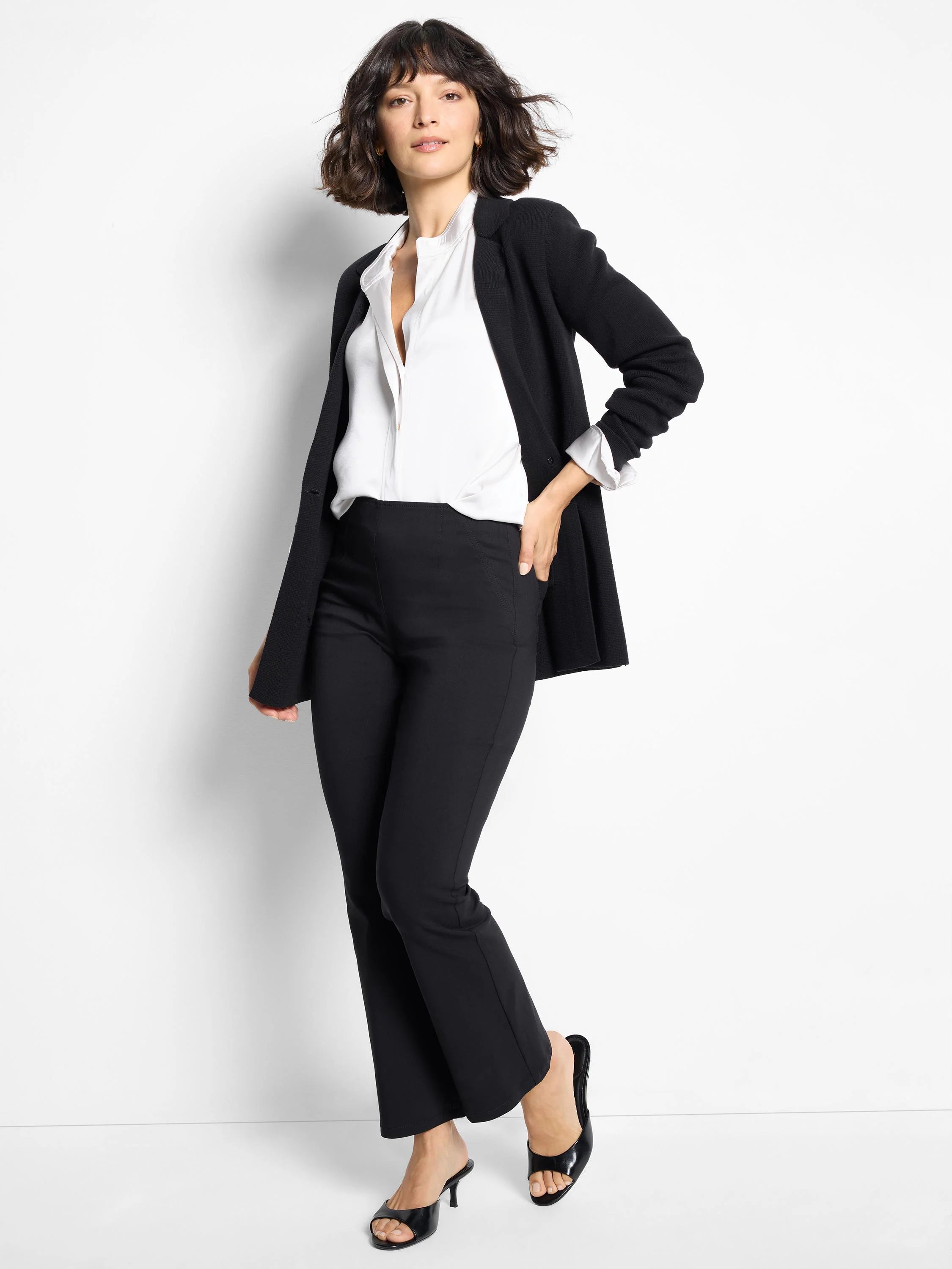 Black knit blazer with an open, relaxed front and long sleeves. Worn over a white shirt.