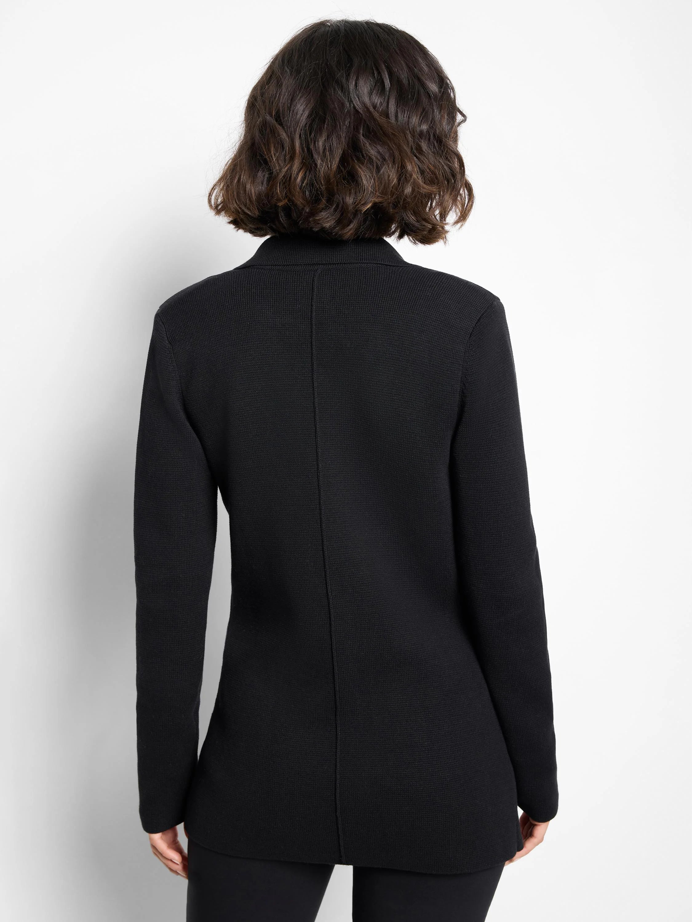 Black blazer, back view on model. Features long sleeves, a structured collar, subtle knit texture, and a central back seam.