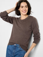 Dark brown crew neck sweater, fine knit texture with ribbed collar, cuffs, and hem. Modeled with blue jeans.