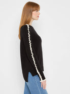 Black sweater with cream ruffled trim running vertically along each outer sleeve.