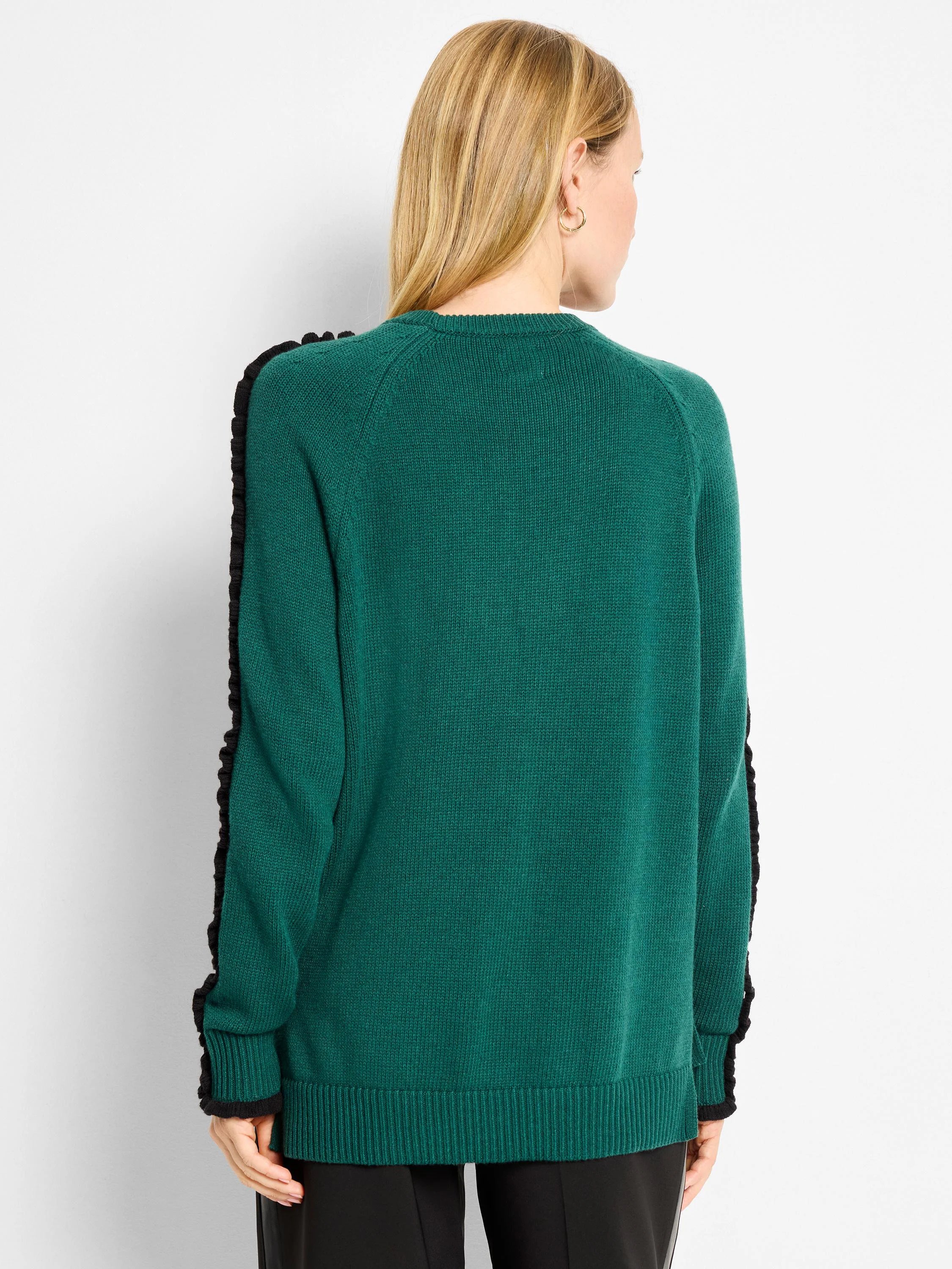 Dark green knit sweater with black ruffles on sleeves, black ribbed cuffs and hem, modeled from the back.