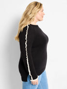 Black sweater with white ruffles along the sleeves and cuffs.