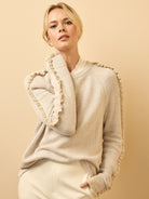 Light beige knit sweater with ruffles along the raglan sleeves and neckline, worn by a model.
