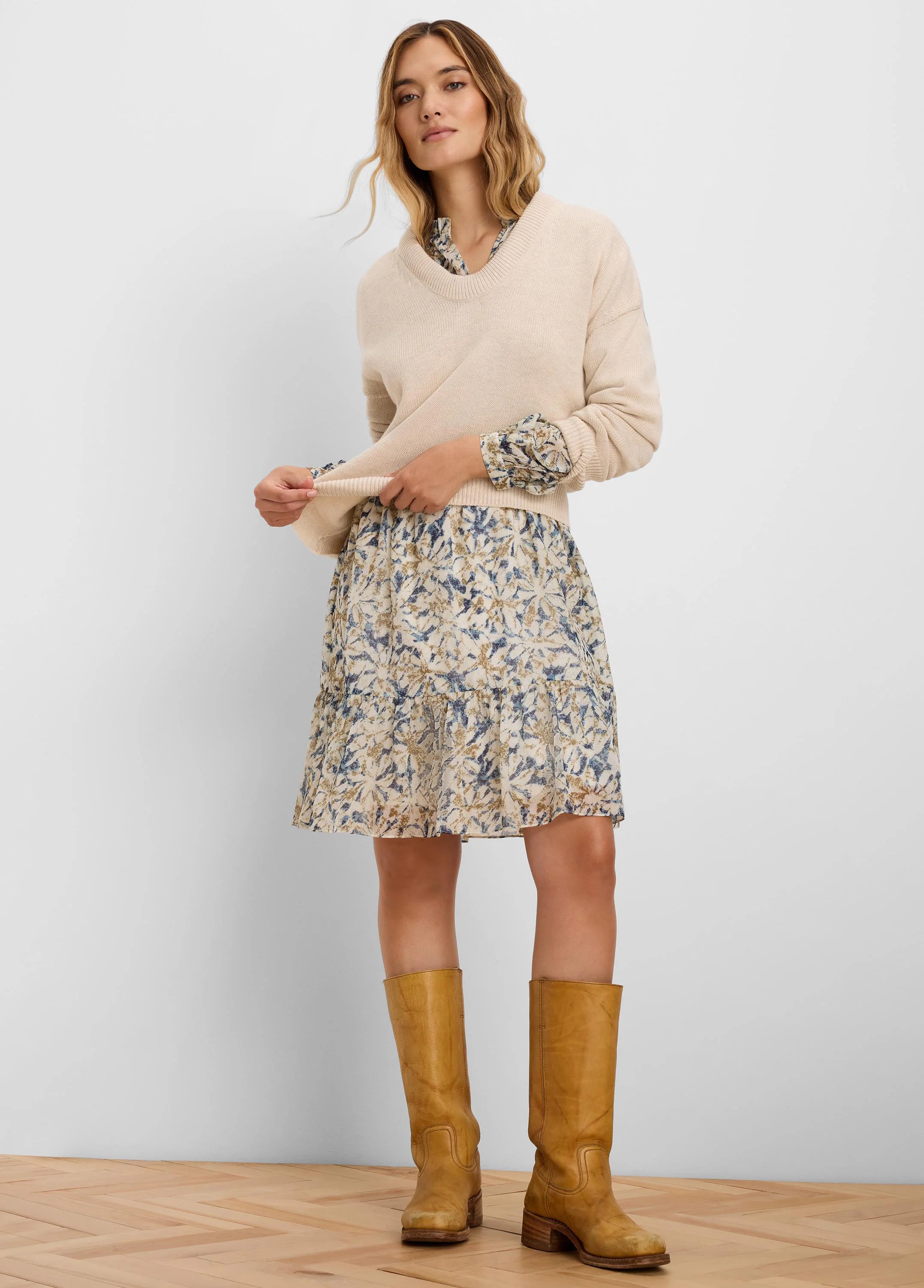 Light beige V-neck sweater, relaxed fit, ribbed cuffs & hem. Model wears it over a patterned dress.