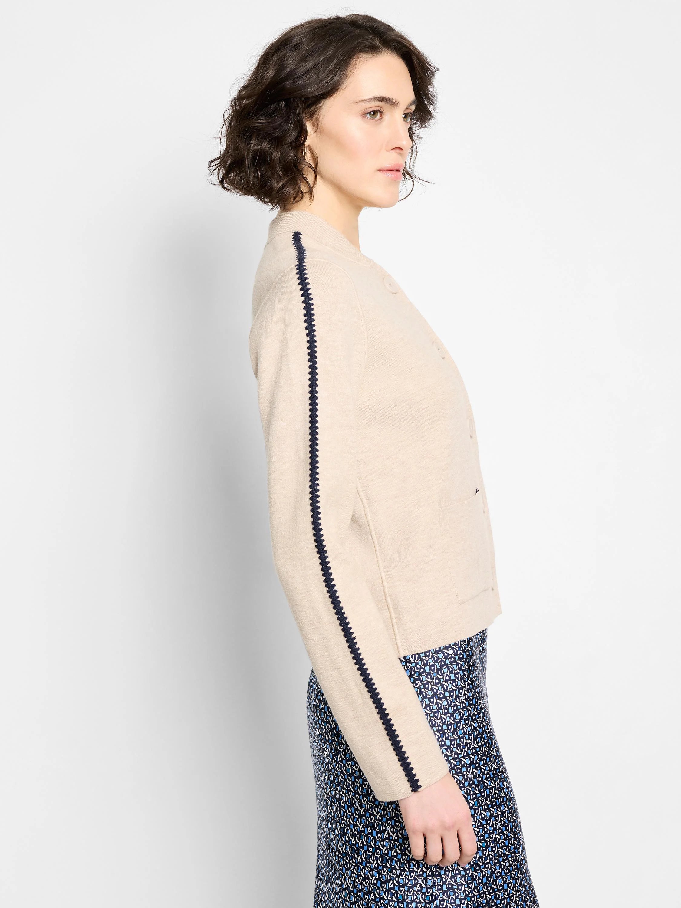 Light beige knit bomber jacket with navy zig-zag sleeve stripes and front buttons.