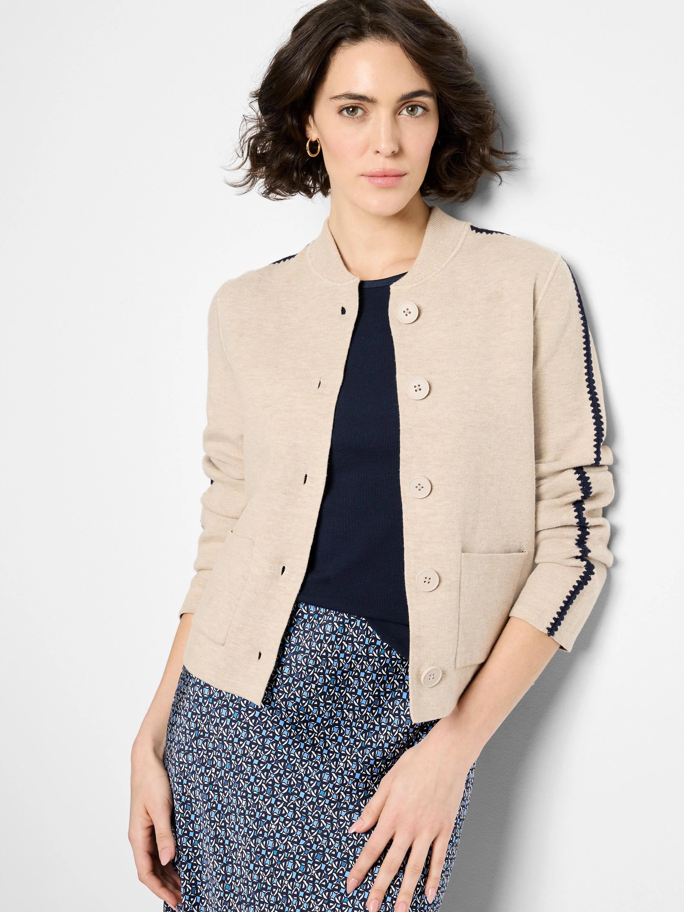 Light beige knit bomber jacket with ribbed collar, button front, navy zigzag sleeve details, and front pockets.