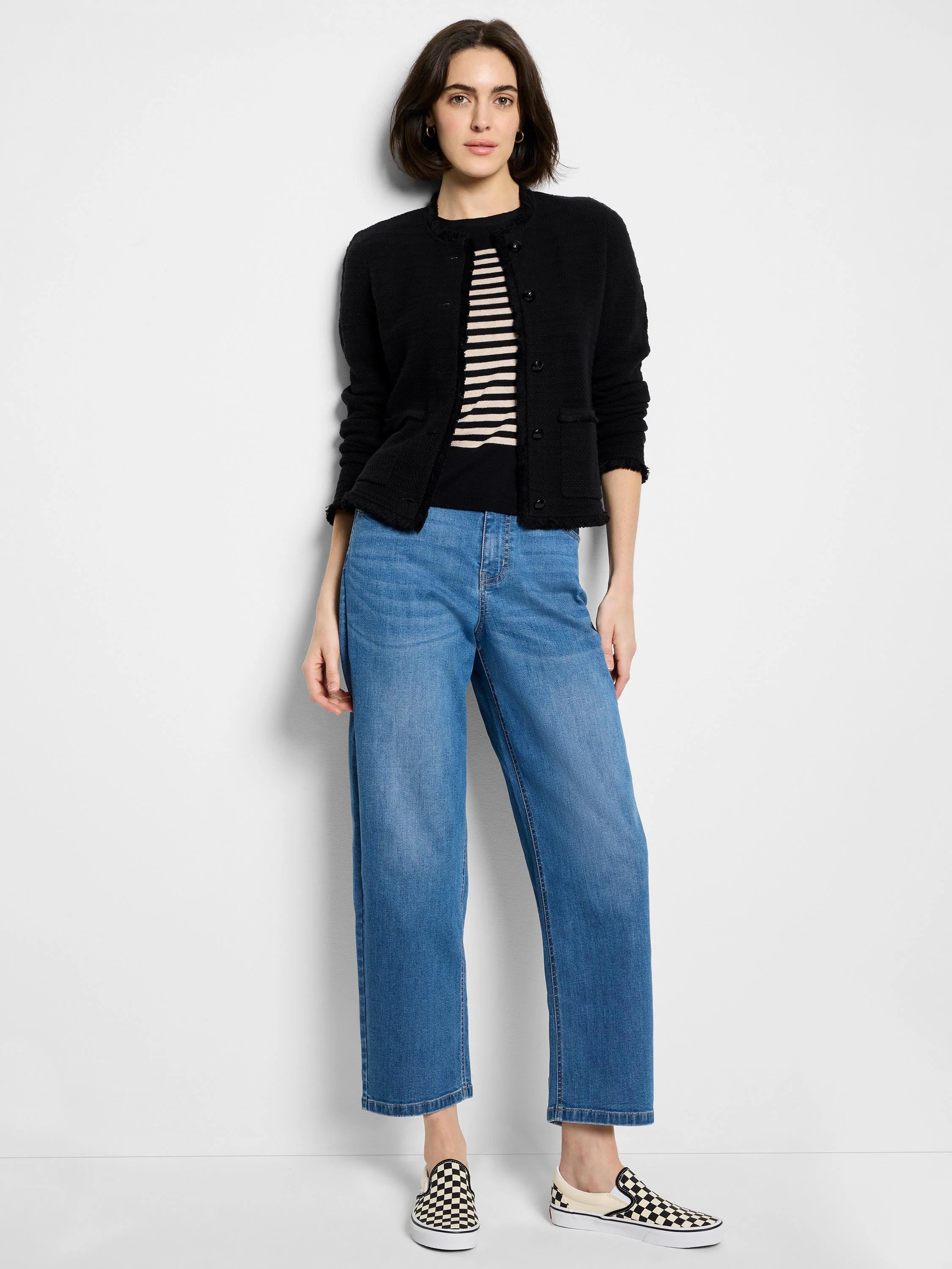 Black knit jacket with frayed edges, button front. Model also wears light wash jeans and checkered slip-on shoes.