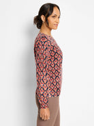 Long-sleeve sweater with an ikat pattern in red, orange, pink, blue, and brown on a dark background.