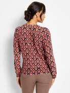 Long-sleeved sweater with red, orange, pink, and blue diamond ikat pattern on dark ground. Model's back.