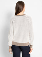 Textured cream sweater with open knit body and brown ribbed collar, cuffs, and hem. Back view.