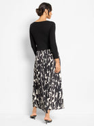 Black ribbed long-sleeve dress with a pleated maxi skirt in an abstract black and off-white print. Back view.