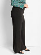 Black wide-leg pants on a model, shown from the side. Features sleek fabric and side pockets.