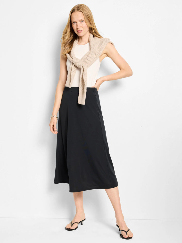 Black midi-length A-line slip skirt. Model wears it with a beige top.