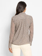 Abstract beige, brown, and black elongated dot pattern on a sheer chiffon top with long sleeves, seen from the back.