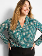Teal V-neck top with cream dots outlined in dark brown, long sleeves with button cuffs.