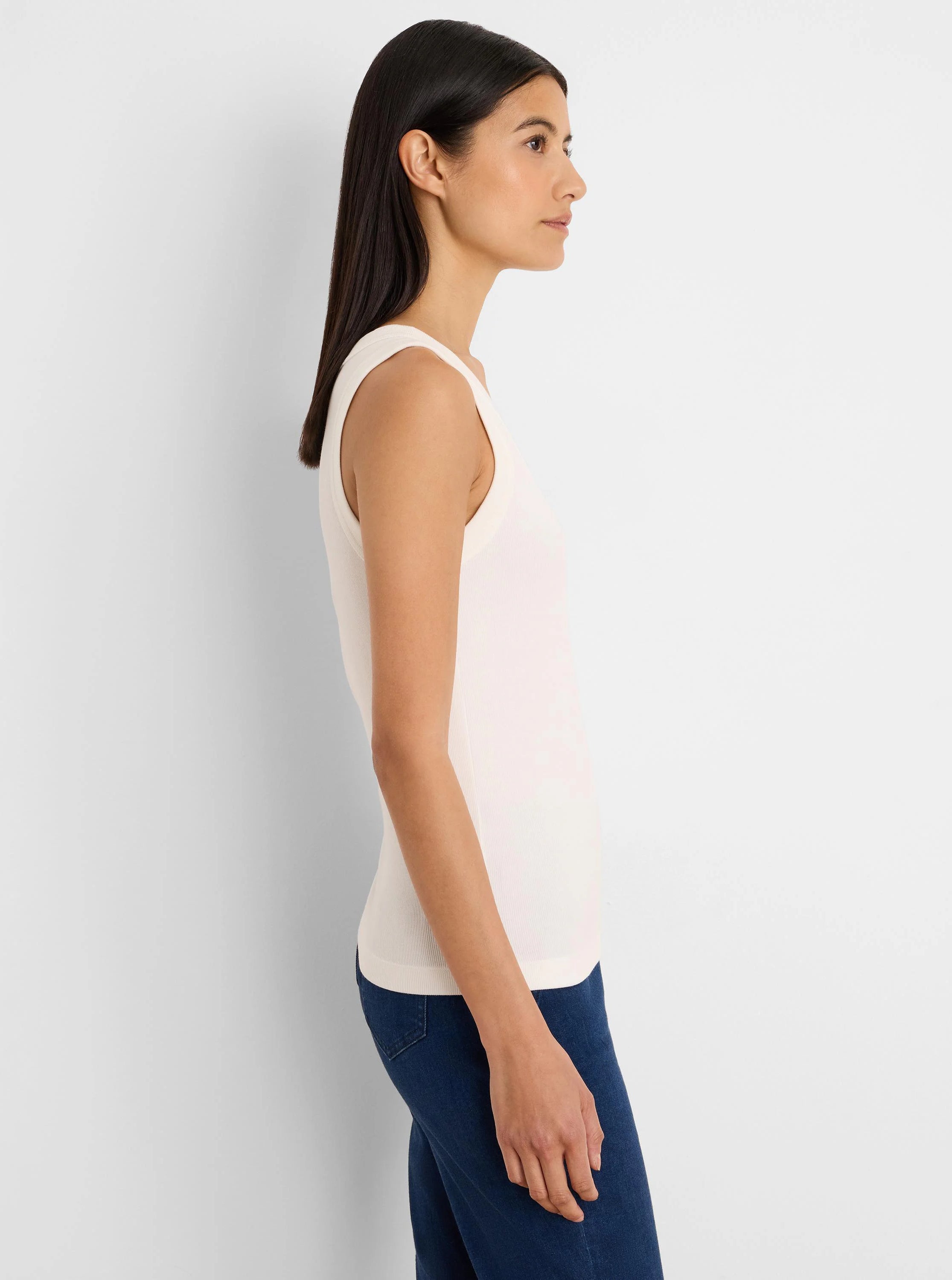 Off-white ribbed scoop neck tank top, worn by a model in profile. Dark blue jeans are visible.