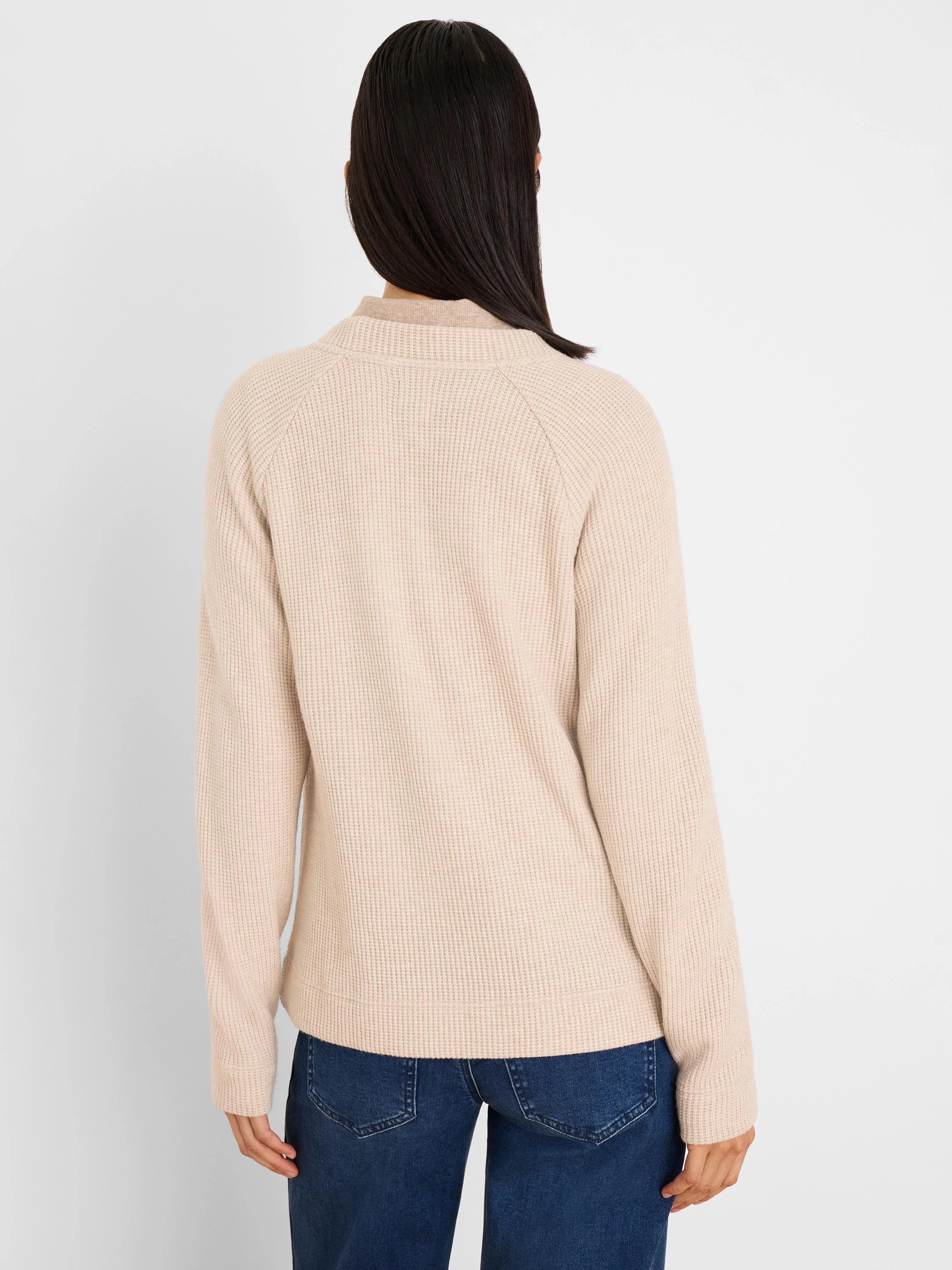 Back view of a model in a light beige waffle knit top with long raglan sleeves and a mock neck.