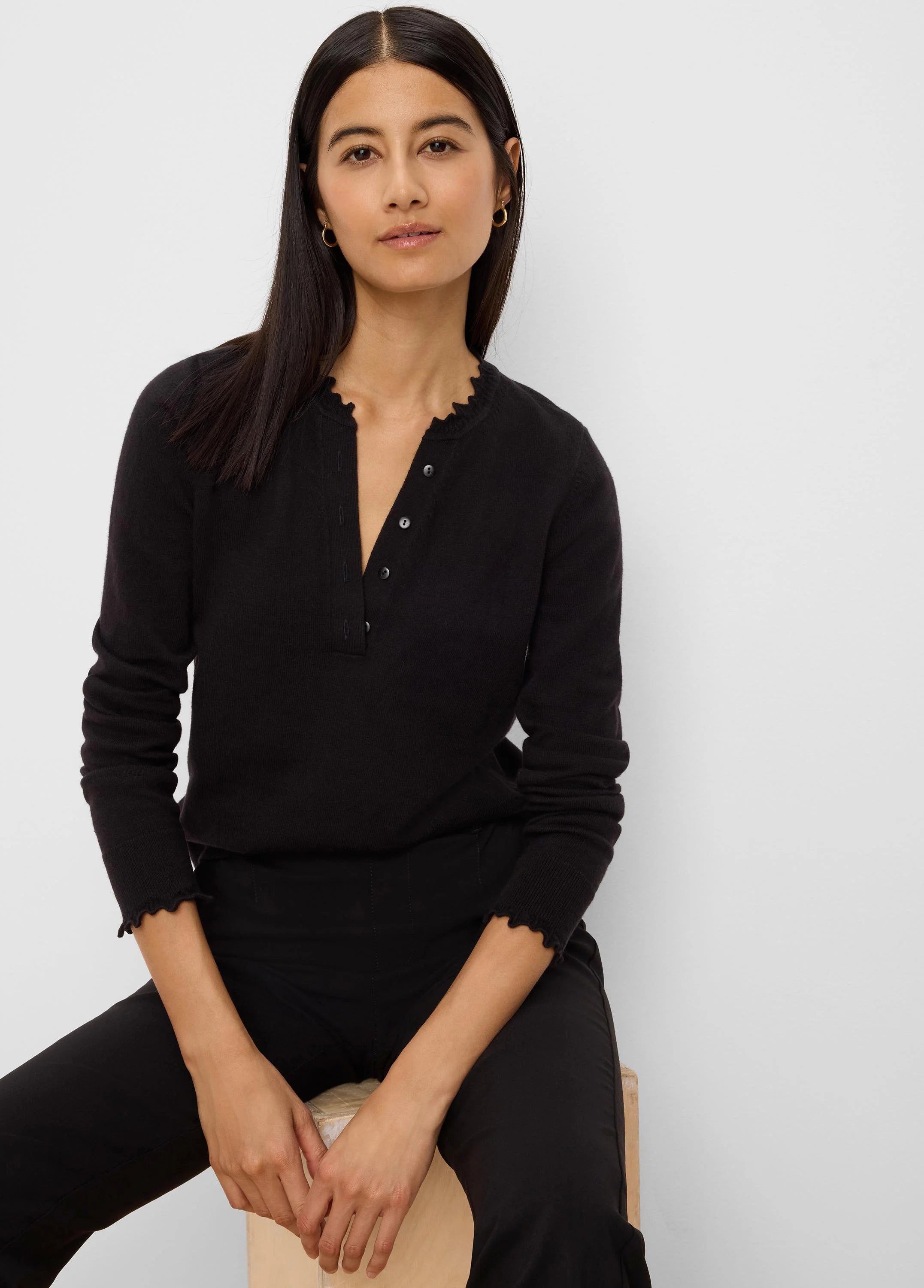 Black Henley sweater with button placket, ruffled neckline, and ruffled cuffs.