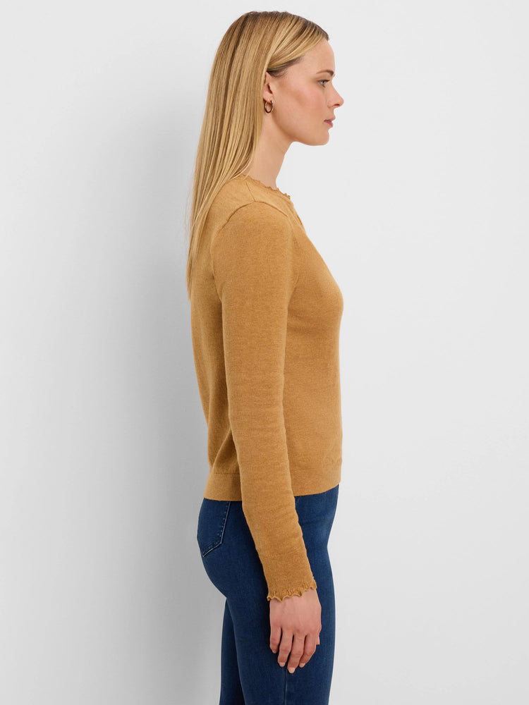 Tan sweater with long sleeves and ruffled neckline and cuffs. Worn by a model in profile.