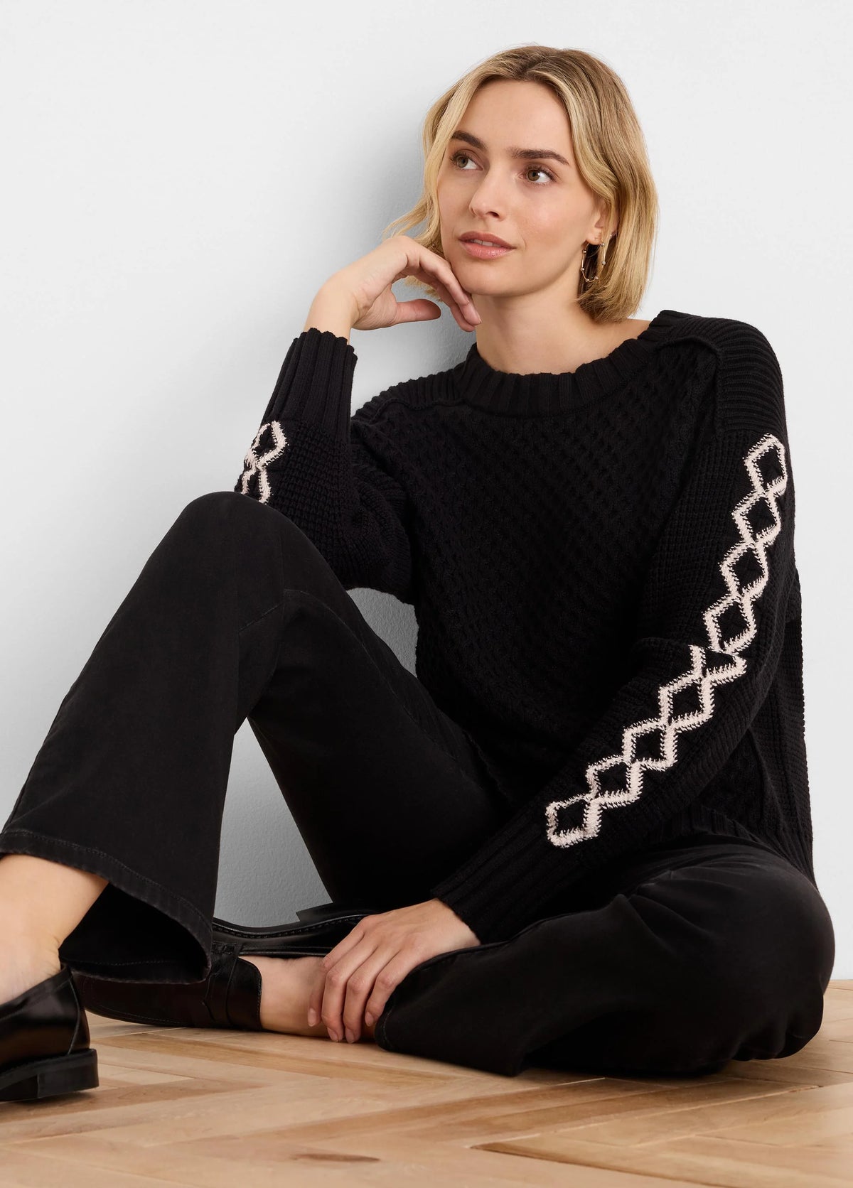 Black textured knit sweater with cream criss-cross diamond patterns running down the sleeves.